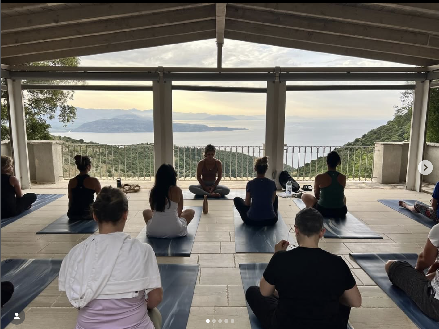 Retreat guests seated on yoga mats with Adriana in an open-air shala overlooking the Greek sea