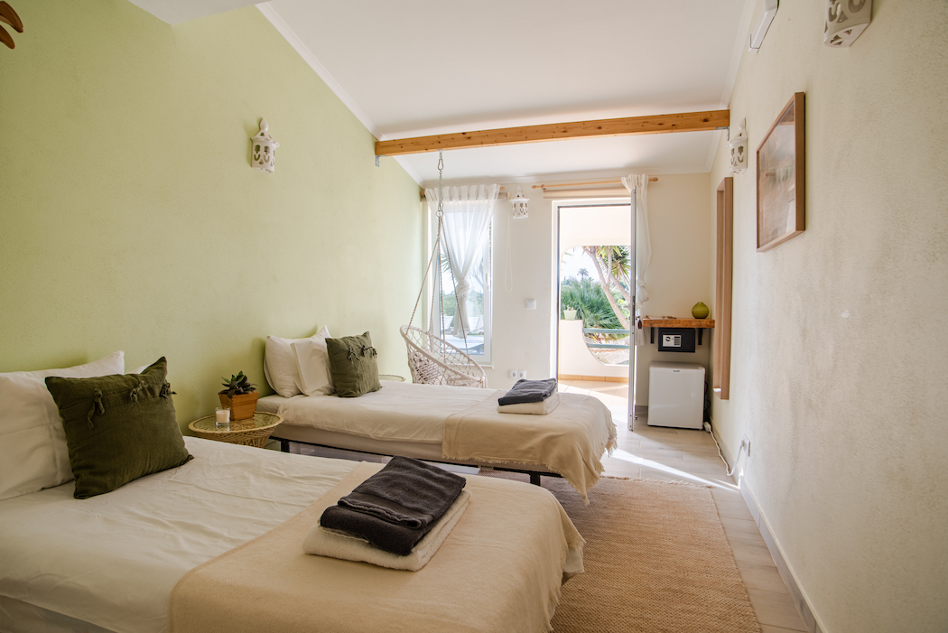 Airy twin bedroom with soft green walls and a hanging chair